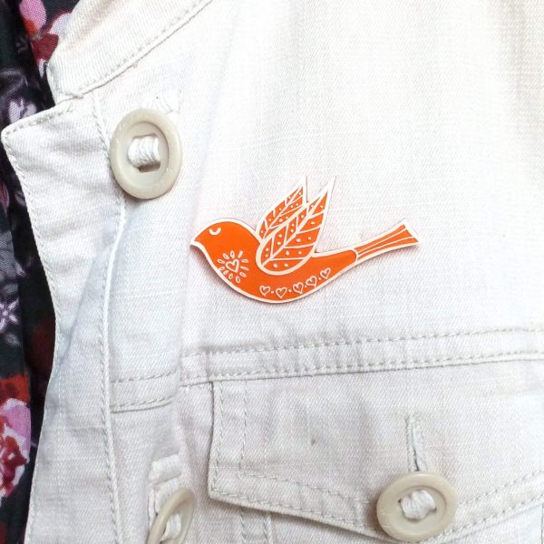 Orange folk art style bird brooch on jacket