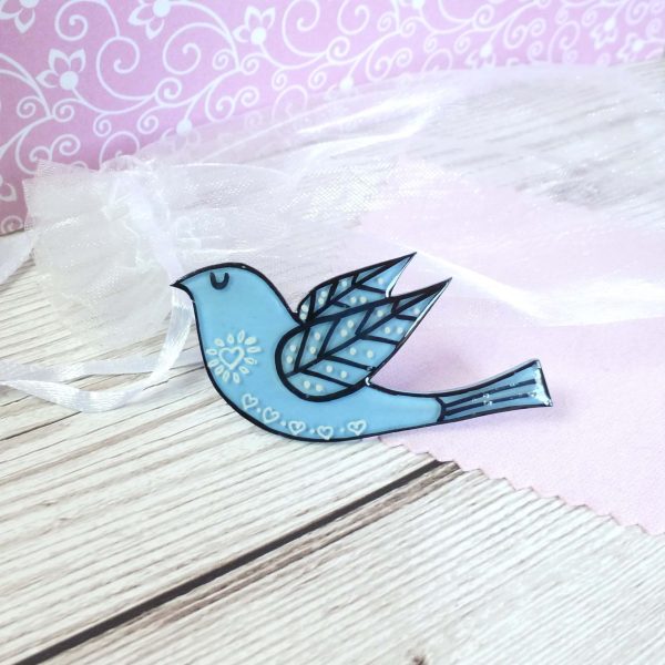 Pale blue folk art style bird brooch on pink background