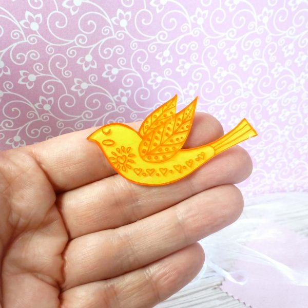 Golden yellow folk art style bird brooch on hand