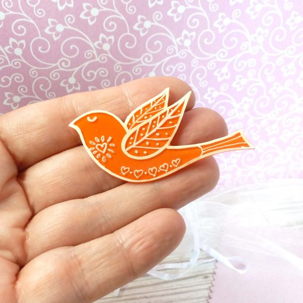 Orange folk art style bird brooch on hand