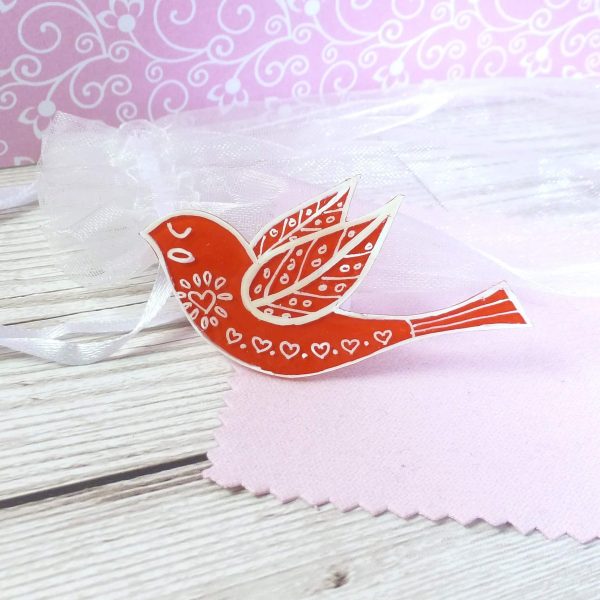 Red folk art style bird brooch on pink background