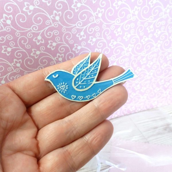 Blue folk art style bird brooch on hand