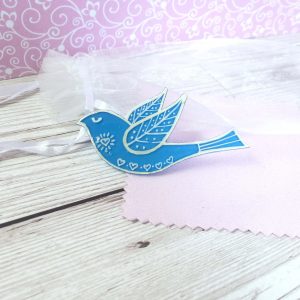 Blue folk art style bird brooch on pink background