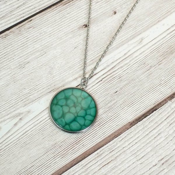 Turquoise 25mm steel pendant on wooden background